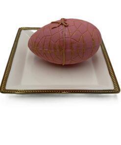 Pink oval soap with a lattice pattern tied with a beige string, placed on a white plate with a gold decorative rim.