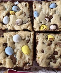 Four square cookie bars with a crumbly, pale top, studded with colorful candy-coated chocolates and melted chocolate pockets.