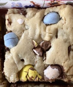 Square cookie bar with pale dough and blue candy-coated chocolates, studded with chocolate chunks.